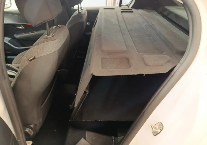 Vue intérieure côté droit du coffre ouvert de la Peugeot 208 blanche, montrant le rangement sous la tablette arrière.