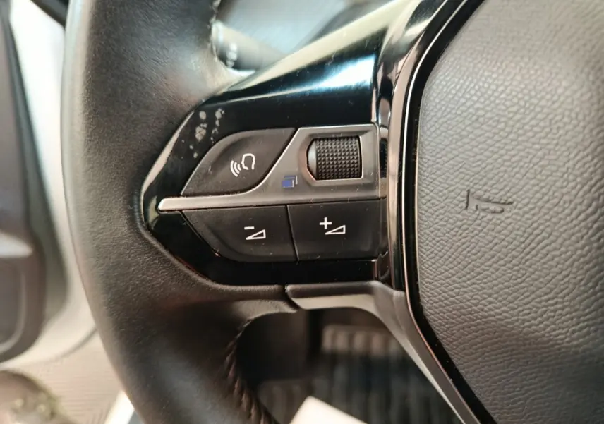 Gros plan sur les commandes gauche du volant cuir noir de la Peugeot 208 1.5 BlueHDi 2023.