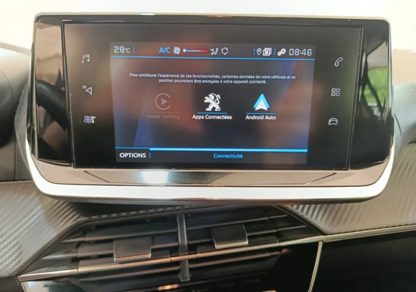 Écran tactile central de la Peugeot 208 2023 affichant Apple CarPlay et Android Auto, avec tableau de bord noir et détails carbone.