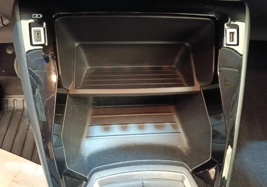Gros plan sur le rangement central noir brillant de la Peugeot 208 blanc, avec ports USB visibles de chaque côté.