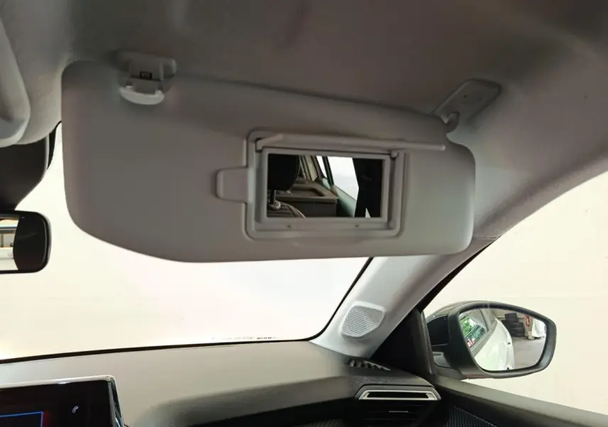 Vue intérieure côté passager du pare-soleil avec miroir ouvert sur Peugeot 208 blanc 2023, tableau de bord et rétroviseur visibles.