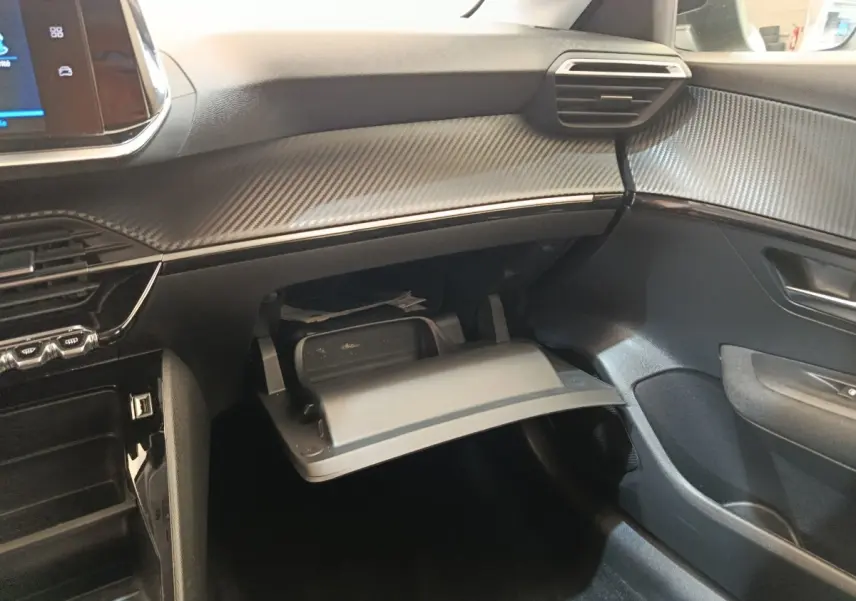 Intérieur de la Peugeot 208 1.5 BlueHDi 2023, vue côté passager sur boîte à gants ouverte et tableau de bord noir texturé.