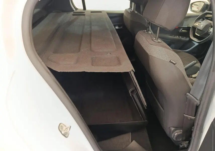 Vue intérieure arrière droite d’une Peugeot 208 blanche 2023, montrant la banquette rabattue et le siège avant en tissu gris.