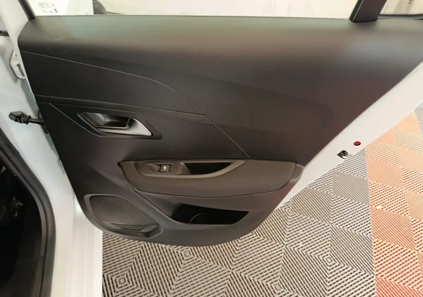Vue rapprochée de la porte arrière gauche blanche de la Peugeot 208 2023 avec panneau intérieur noir et commande de vitre.