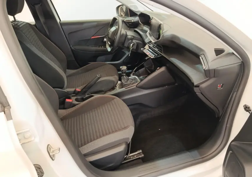 Intérieur avant droit de la Peugeot 208 blanche, montrant sièges tissu noirs et tableau de bord avec écran tactile.