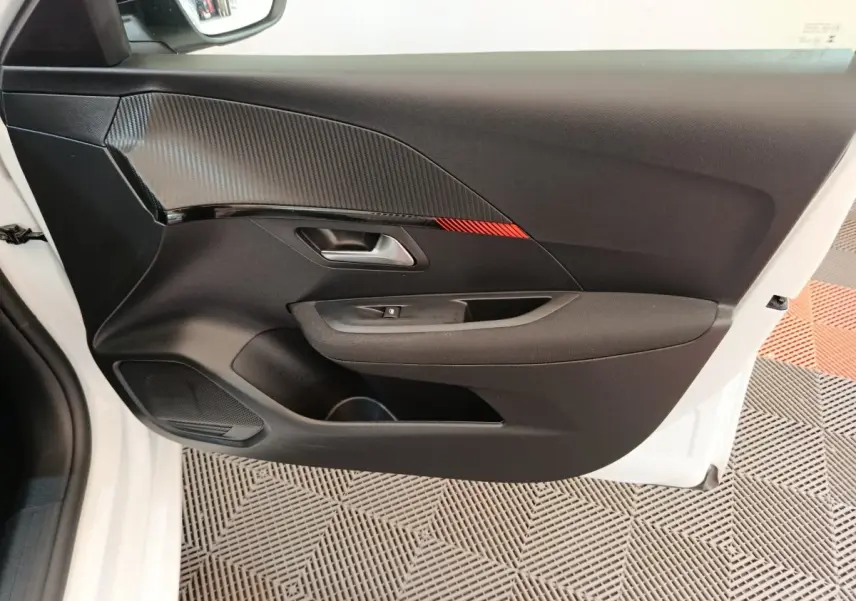 Vue intérieure de la porte avant gauche noire avec insert décoratif rouge de la Peugeot 208 blanche 2023.