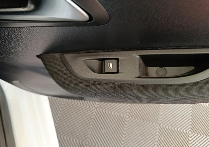 Détail du bouton de commande de lève-vitre sur la porte côté gauche d'une Peugeot 208 blanche 2023.