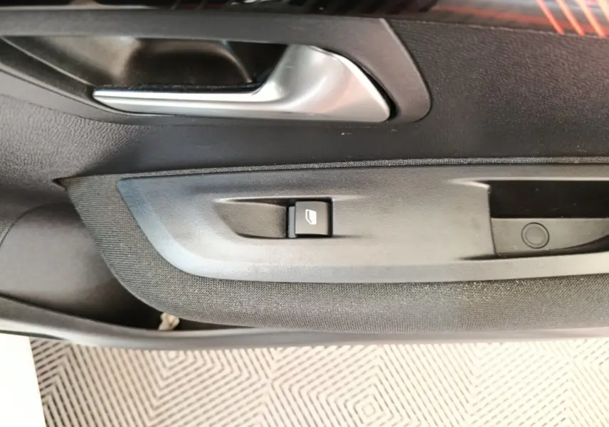Gros plan sur la poignée intérieure et le bouton de lève-vitre côté gauche de la porte d’une Peugeot 208 blanche.