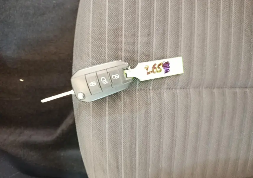 Clé de voiture Peugeot 208 posée sur un siège tissu gris foncé à rayures verticales.