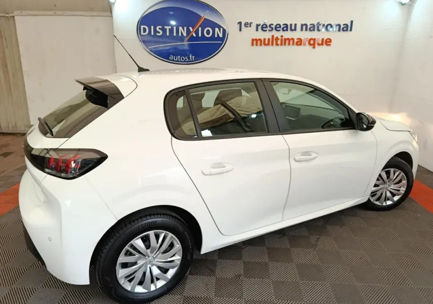 Vue 3/4 arrière droite d'une Peugeot 208 blanche 2023 dans un showroom avec jantes alliage et feux arrière LED.