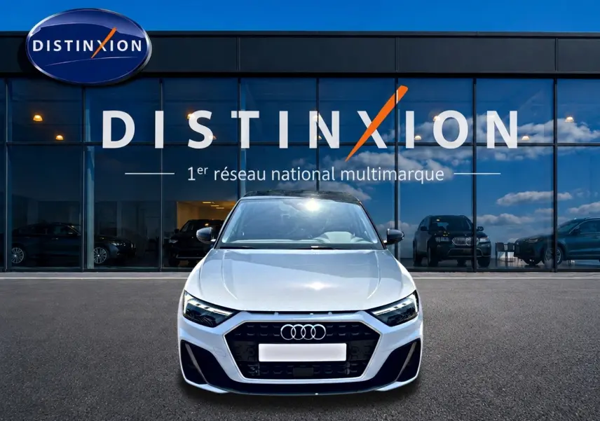 Vue avant d'une Audi A1 Sportback 30 TFSI blanche avec calandre noire et logo Audi, devant une vitrine Distinxion.