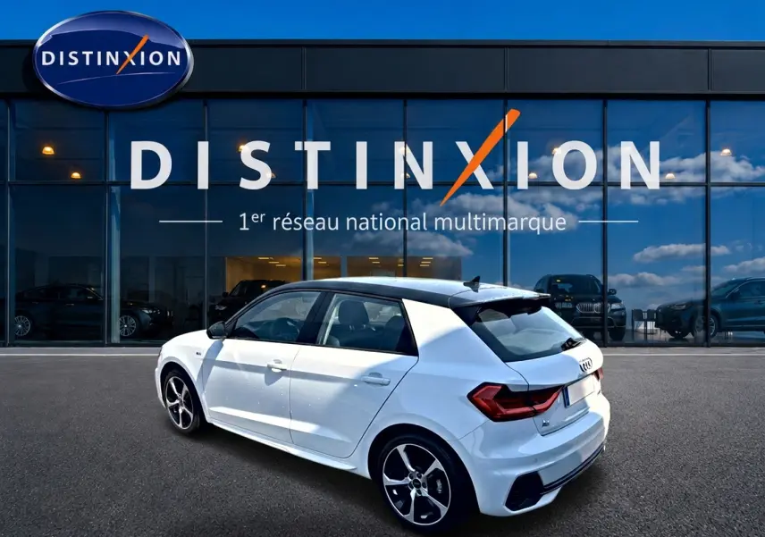 Audi A1 Sportback blanc avec toit noir en 3/4 arrière droit, jantes alu et becquet arrière visible devant showroom Distinxion.