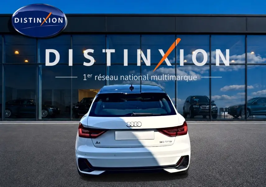 Vue arrière d'une Audi A1 Sportback blanche avec toit noir, feux LED et becquet arrière, stationnée devant un showroom Distinxion.