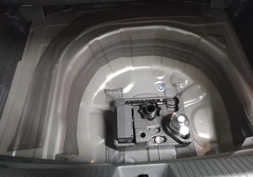 Gros plan sur le compartiment de rangement sous le coffre du Volkswagen Taigo gris cendré, montrant l’emplacement de la roue de secours.