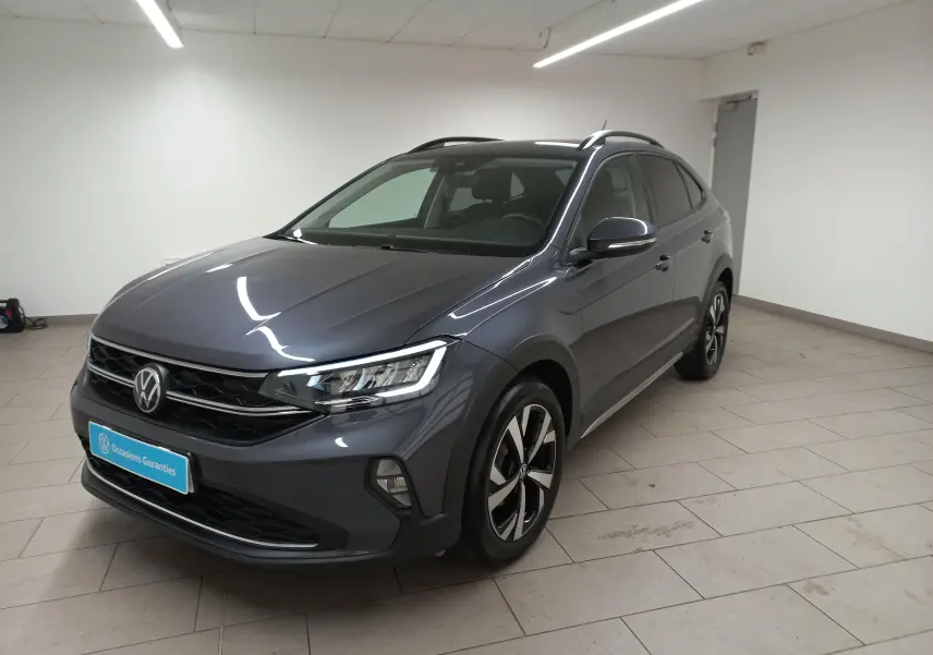 Volkswagen Taigo gris cendré en 3/4 avant droit, avec jantes alliage et projecteurs LED antibrouillard visibles.