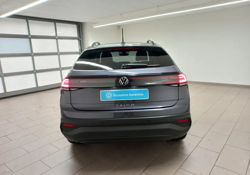 Vue arrière d'un Volkswagen Taigo gris cendré 2025 avec feux LED allumés dans un garage lumineux.