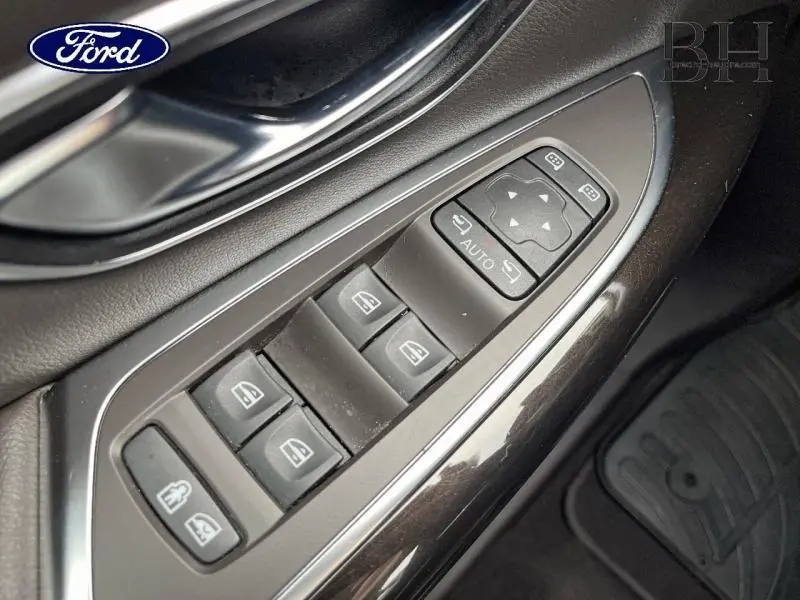 Gros plan sur les commandes de lève-vitres et rétroviseurs côté conducteur en plastique noir brillant.