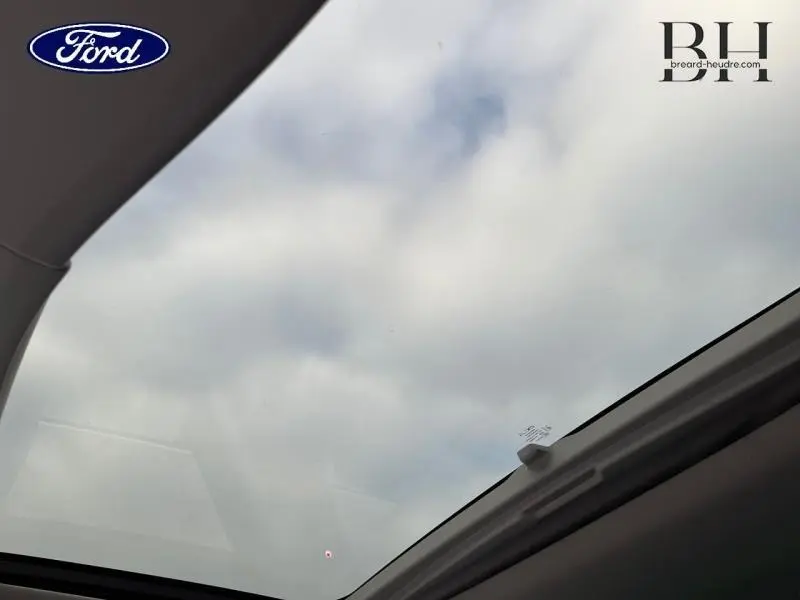 Vue intérieure du toit ouvrant panoramique électrique du Renault Espace gris Cassiopée, montrant le ciel nuageux au-dessus.