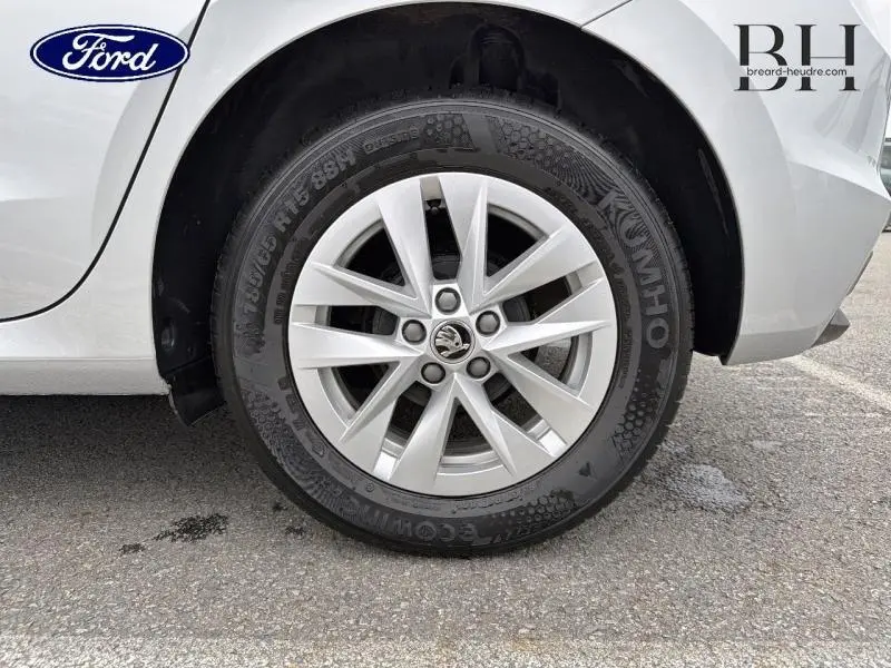 Gros plan sur la roue arrière droite d'une Skoda Fabia gris argent métallisé avec jante alu et logo Skoda visible.