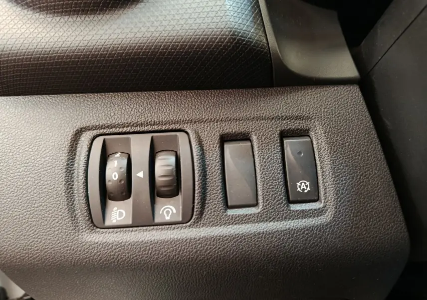 Gros plan sur les commandes de réglage des phares et de l'éclairage intérieur côté gauche d'une Renault Clio blanche 2018.