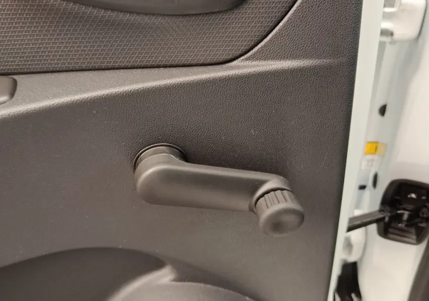Détail de la manivelle de lève-vitre côté gauche sur porte intérieure noire d’une Renault Clio Business dCi 75 blanche.