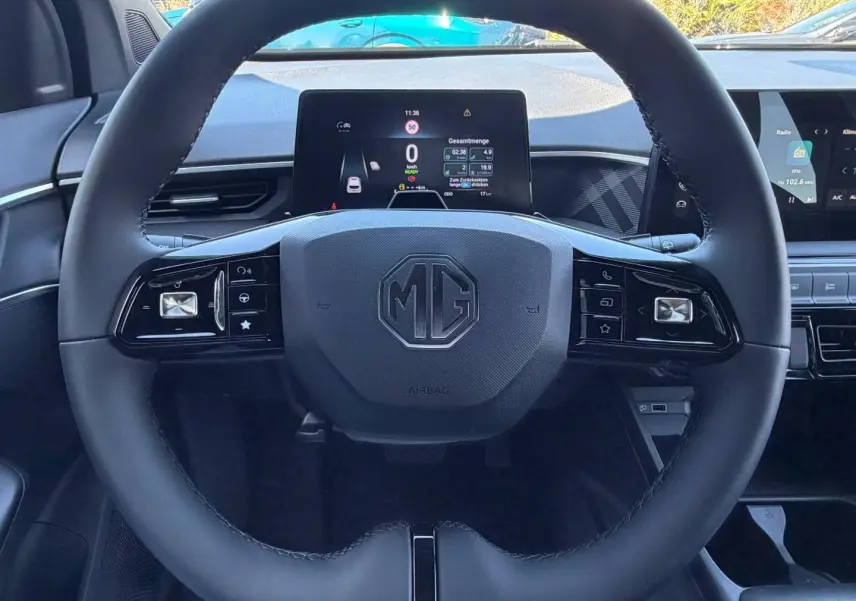 Vue centrée sur le volant cuir multifonction avec logo MG, tableau de bord numérique et écran tactile en arrière-plan.