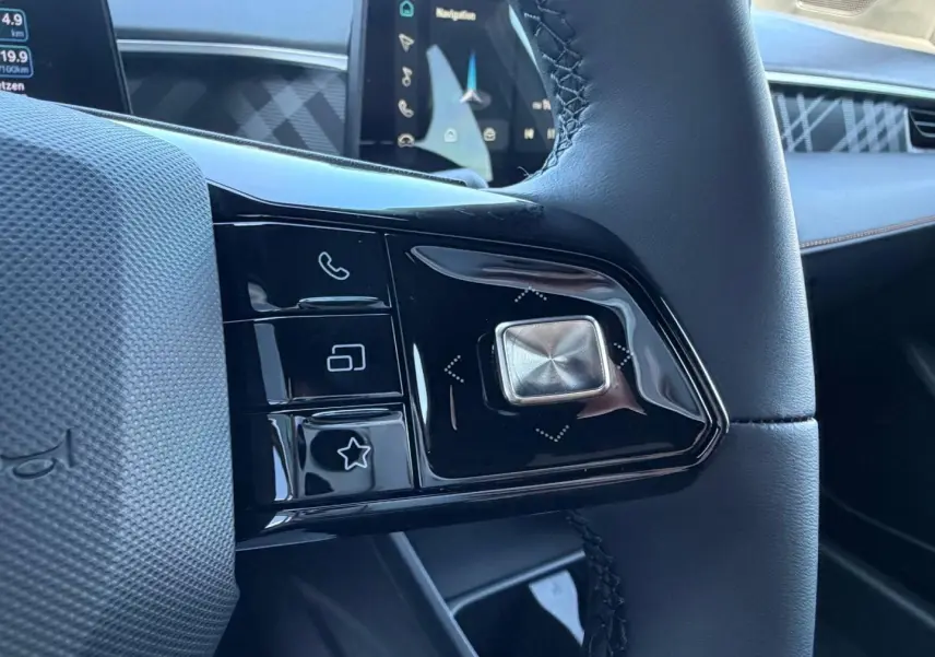 Gros plan sur les commandes noires brillantes du volant cuir noir du MG3 1.5 Hybrid+ Pebble Black, avec écran tactile en arrière-plan.