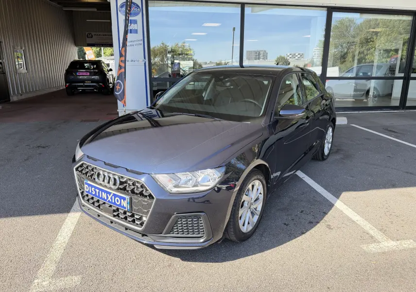 Audi A1 Sportback bleu firmament vue 3/4 avant droit, stationnée devant une vitrine avec plaque Distinxion.