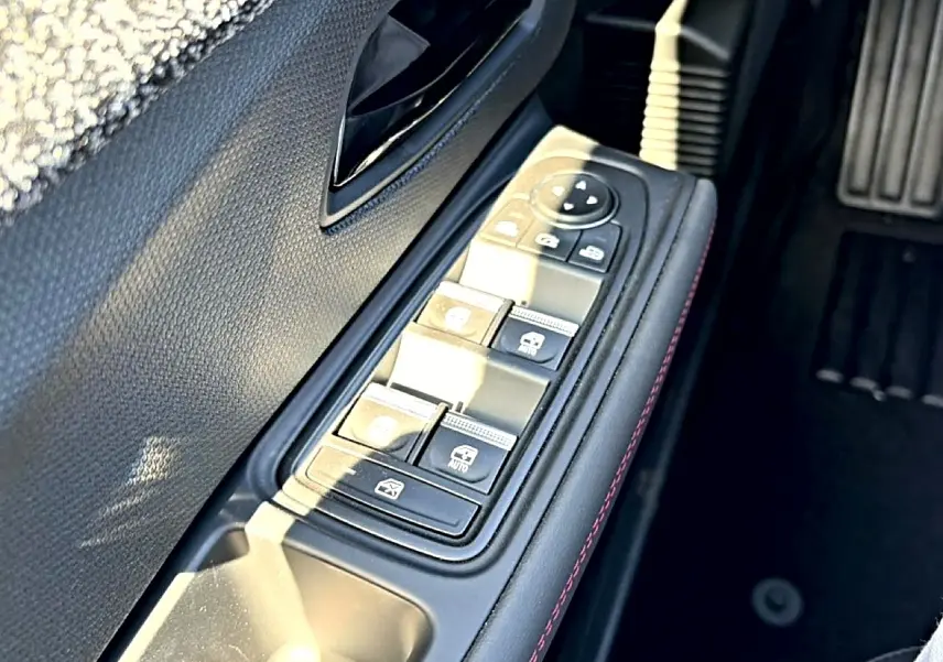 Gros plan sur la commande des vitres électriques côté conducteur avec surpiqûres rouges, intérieur noir de la Renault Clio VI.