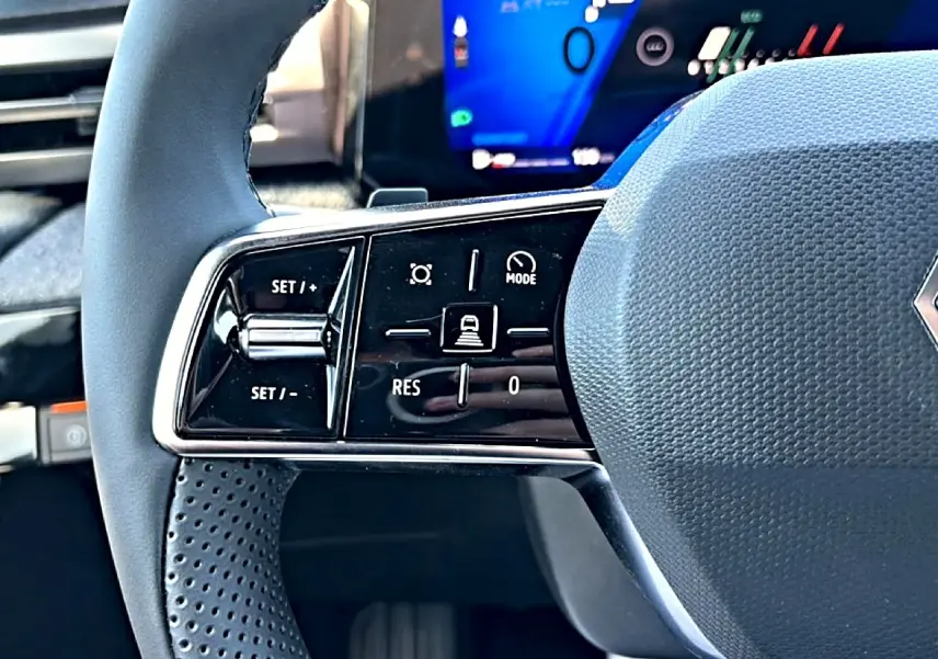 Gros plan sur la partie gauche du volant gris de la Renault Clio VI avec commandes de régulateur de vitesse et écran digital flou en arrière-plan.