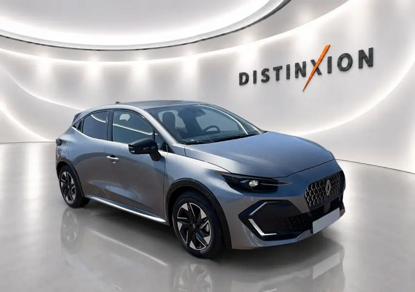 Renault Clio VI gris schiste vue 3/4 avant droit, avec jantes alu et calandre distinctive en showroom lumineux.