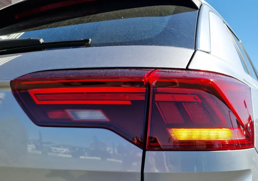 Gros plan sur le feu arrière droit rouge et orange d'un Volkswagen T-Roc gris pyrite 2023 sous un ciel bleu.