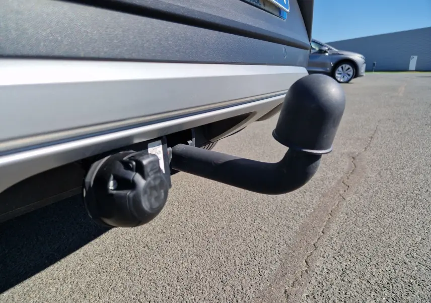 Gros plan sur l'attelage noir fixé au pare-chocs arrière gris pyrite du Volkswagen T-Roc 2023, avec prise électrique visible.