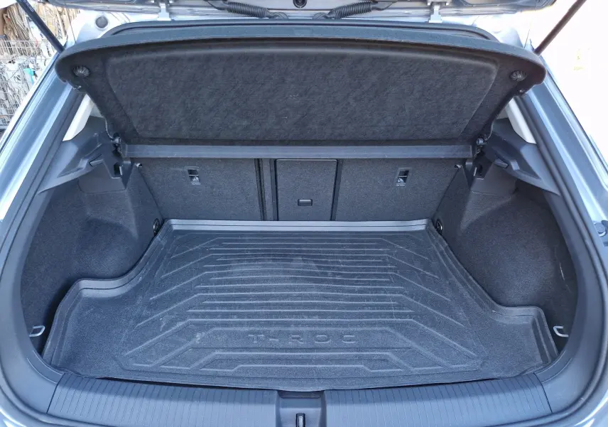 Coffre ouvert vu de l'arrière d'un Volkswagen T-Roc gris Pyrite, avec tapis de coffre marqué T-ROC.