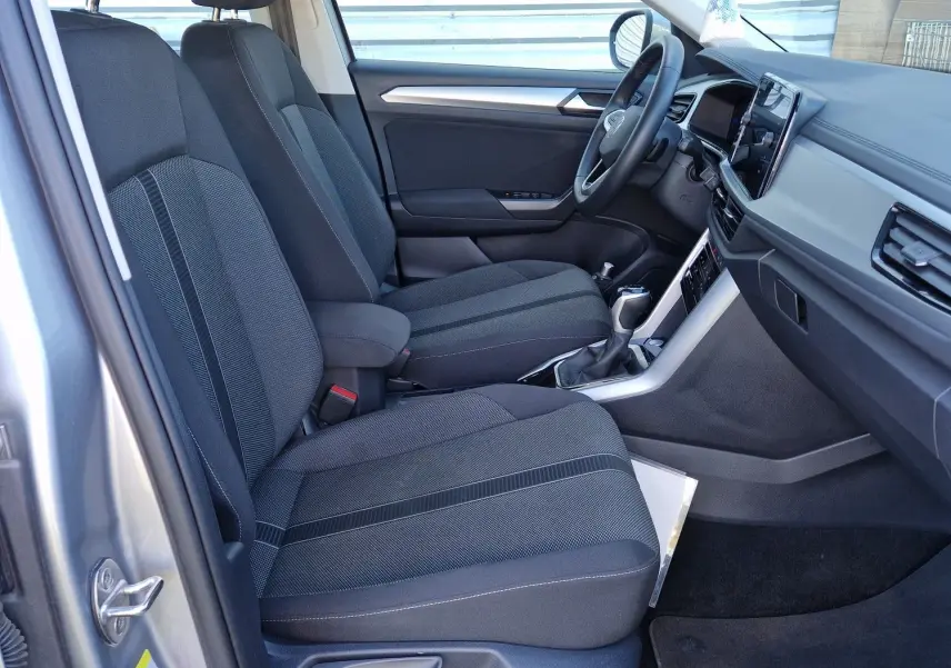 Vue intérieure côté conducteur du Volkswagen T-Roc gris pyrite 2023, mettant en valeur les sièges tissu et le tableau de bord moderne.