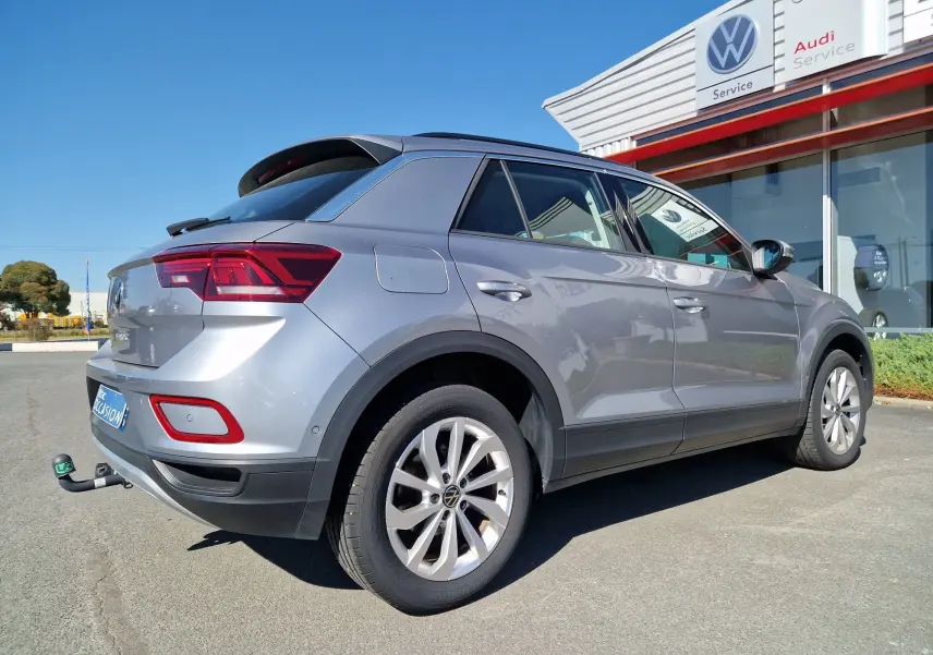 Volkswagen T-Roc gris pyrite vu 3/4 arrière droit avec attelage, stationné devant un service Volkswagen.