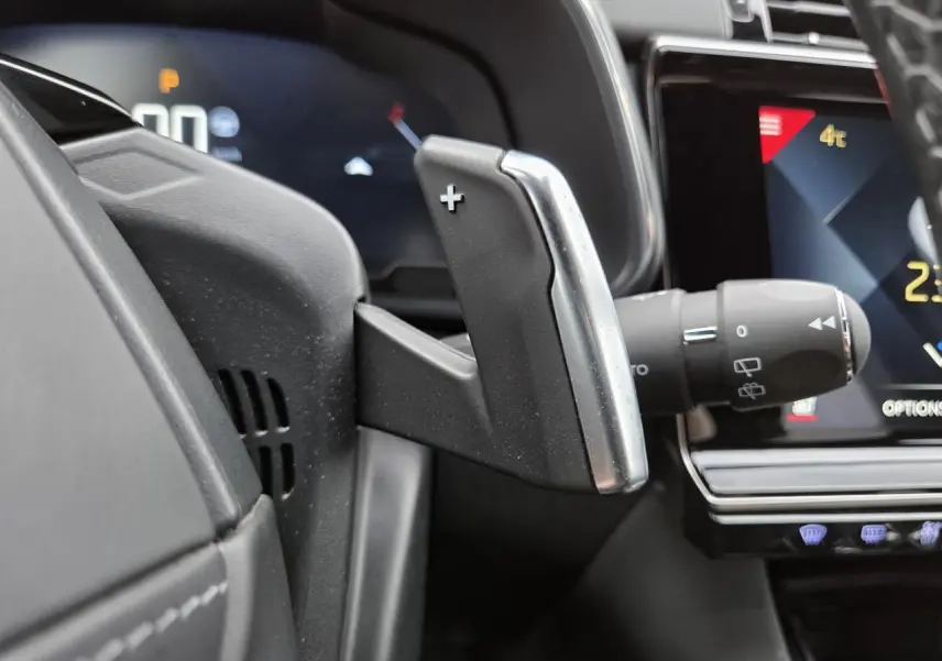 Gros plan sur la palette de changement de vitesse + au volant du DS7 Crossback noir, avec tableau de bord digital en arrière-plan.