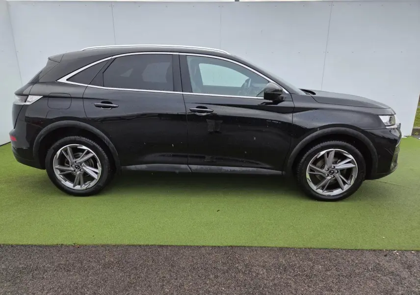 Profil côté gauche du DS7 Crossback noir Perla Metal avec jantes alliage 19 pouces sur fond vert.