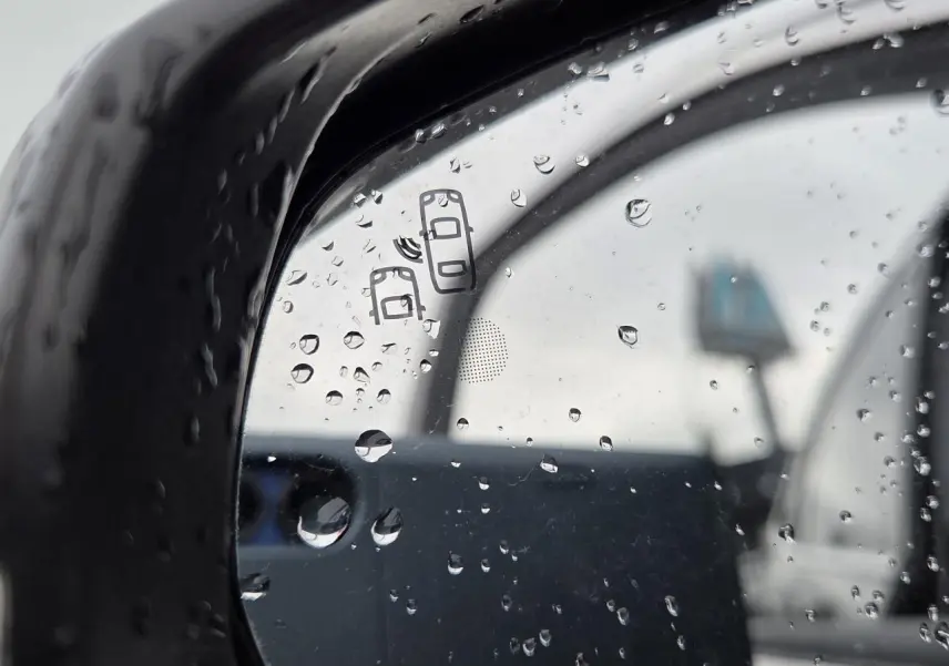 Gros plan sur le rétroviseur côté droit noir perla metal du DS7 Crossback 2022 avec gouttes de pluie et symbole d'alerte d'angle mort.