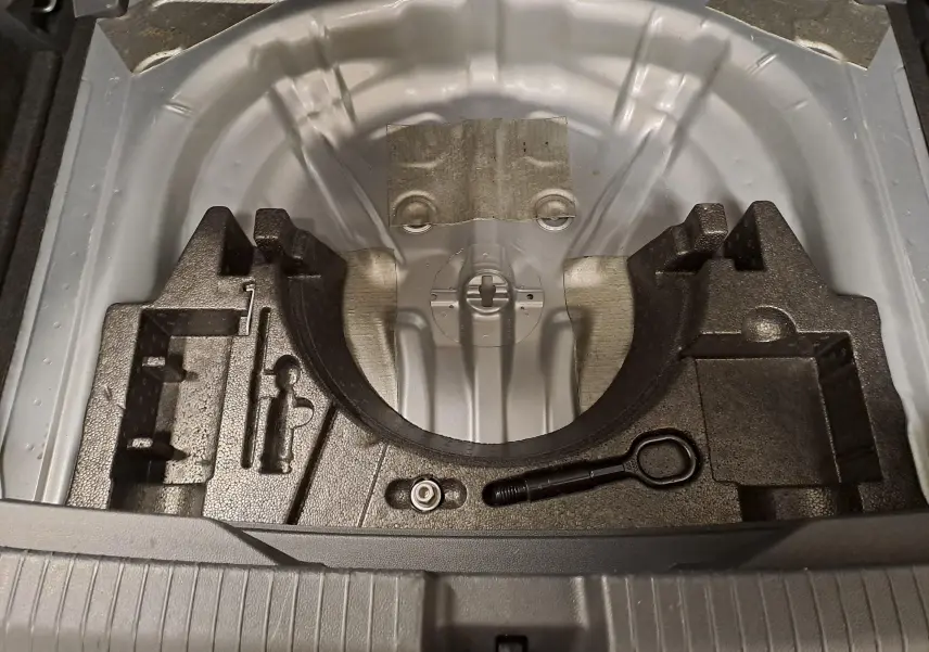 Vue plongeante sur le coffre ouvert du Volkswagen T-Roc gris, montrant le rangement pour roue de secours et outils.