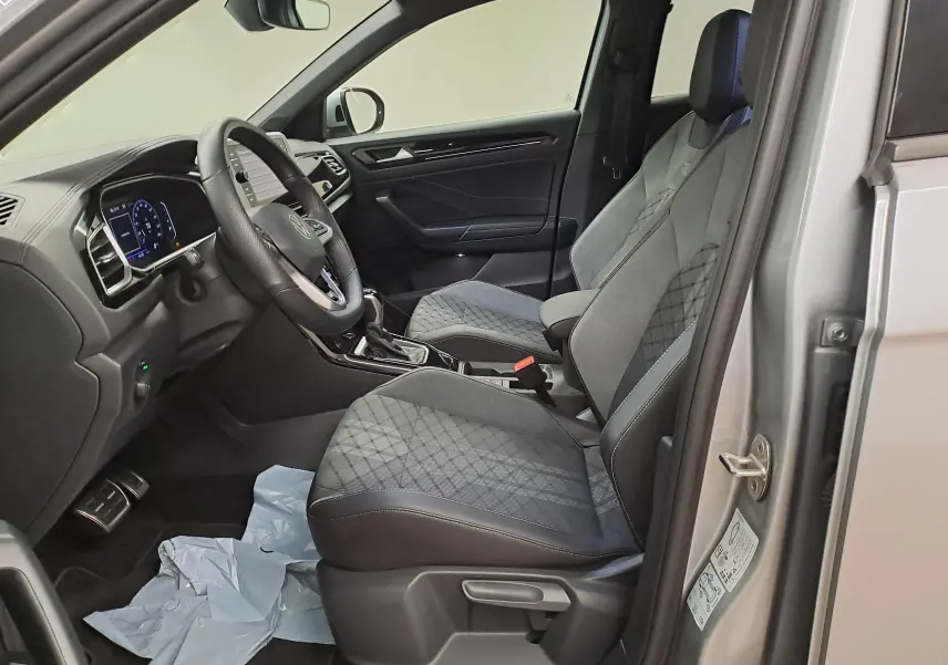 Vue intérieure côté conducteur du Volkswagen T-Roc 1.5 TSI Gris Pyrite, sièges tissu et tableau de bord moderne.