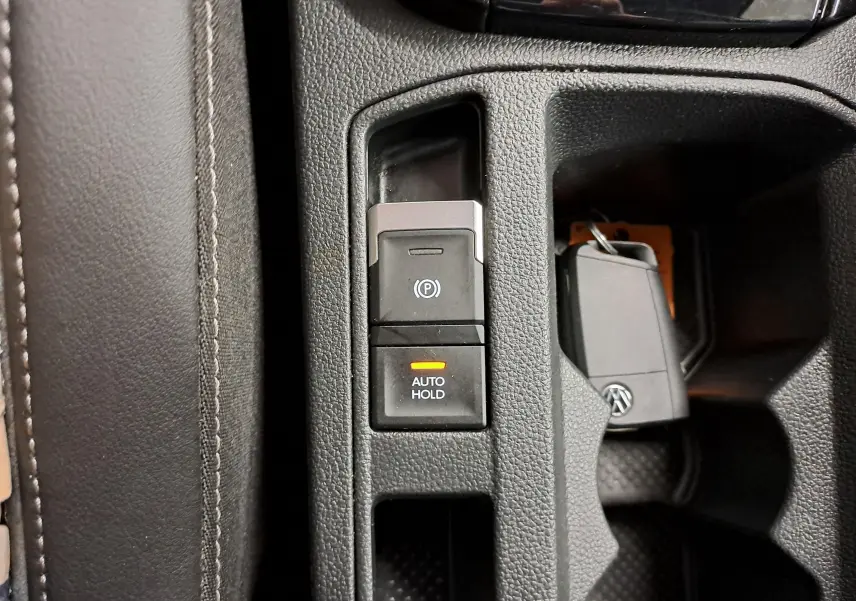 Gros plan sur la console centrale du Volkswagen T-Roc 2025, montrant les boutons frein à main électrique et Auto Hold avec clé VW.