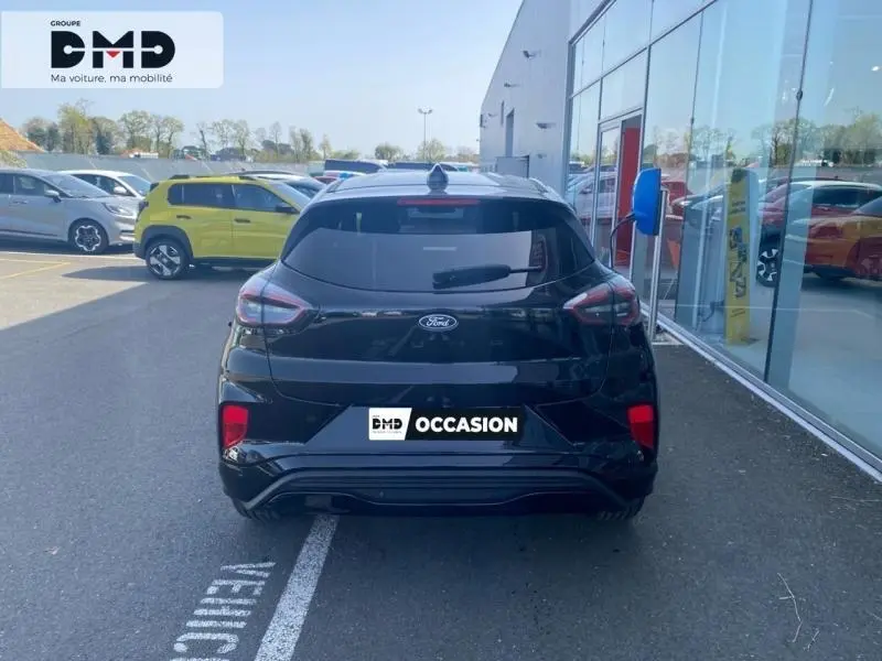 Vue arrière d'un Ford Puma noir Agate Métallisée 2026, avec feux LED et lunette arrière surteintée, stationné devant un bâtiment vitré.
