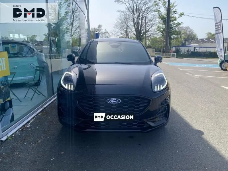Vue avant d'une Ford Puma noir agate métallisée avec phares Matrix LED allumés, stationnée devant une vitrine.