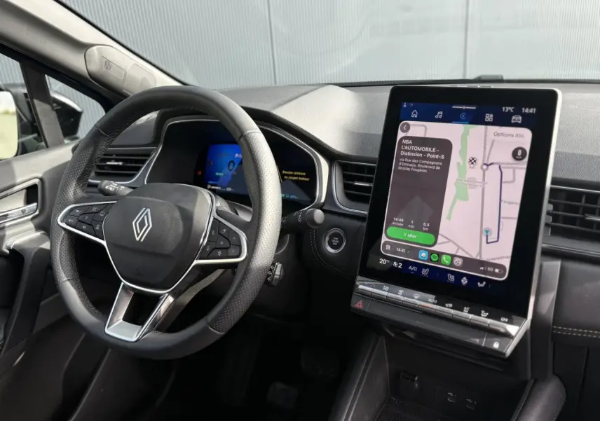 Vue intérieure du poste de conduite Renault Symbioz bleu Iron, avec volant multifonction et grand écran tactile vertical affichant la navigation.