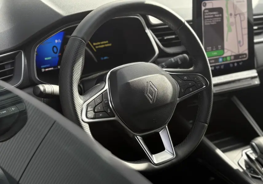 Gros plan sur le volant noir en cuir perforé du Renault Symbioz 2025 avec tableau de bord numérique et écran tactile GPS.