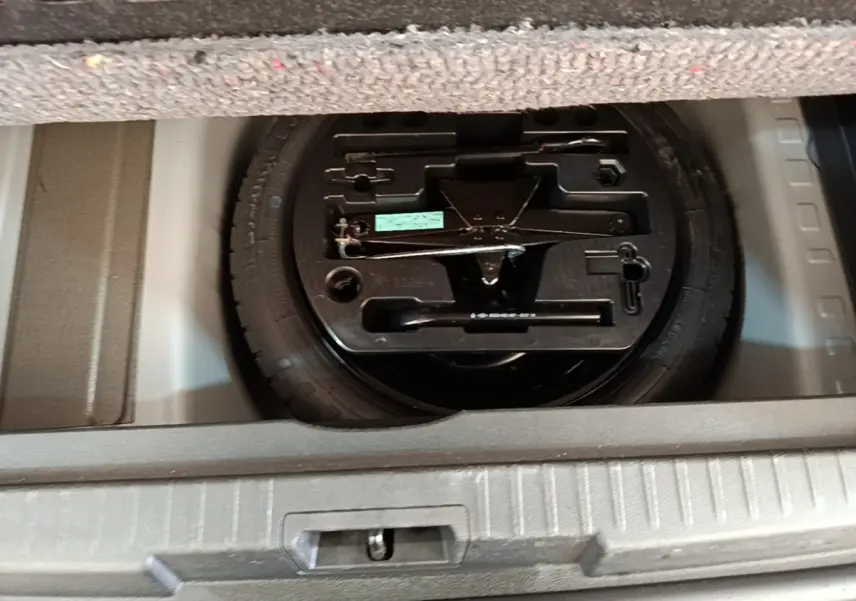 Vue rapprochée du coffre ouvert du Renault Captur gris clair 2018, montrant la roue de secours et son outillage.