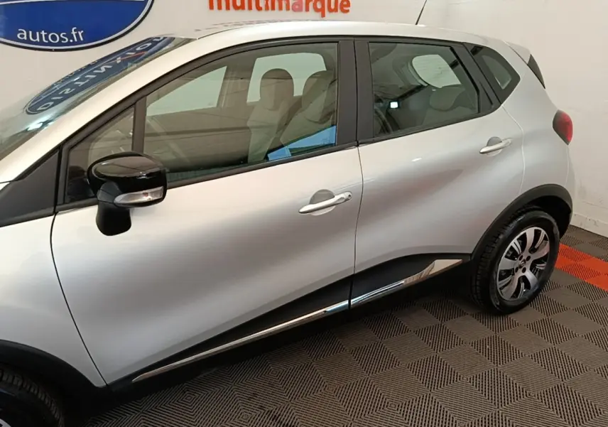 Vue latérale côté gauche d’un Renault Captur gris clair 2018 avec rétroviseurs noirs et jantes alliage.