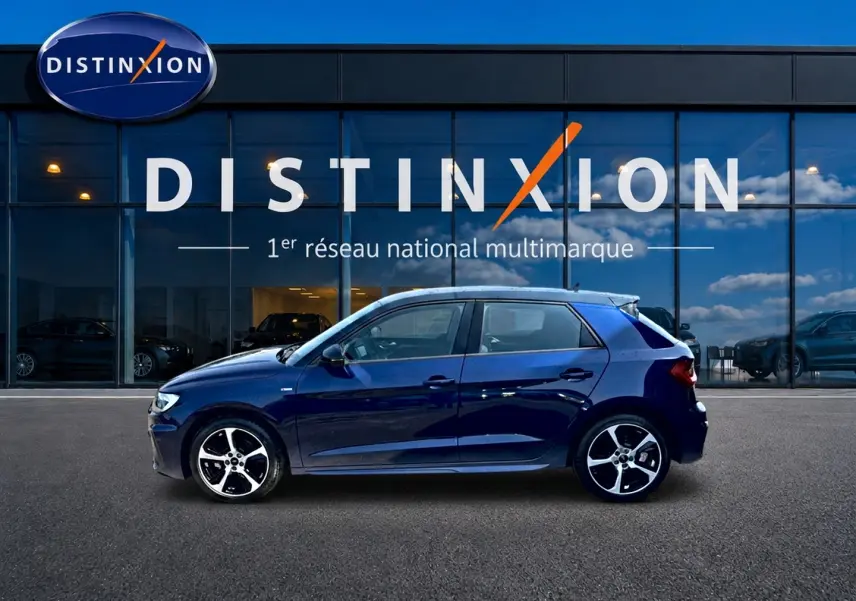 Profil côté gauche de l'Audi A1 Sportback 30 TFSI bleu foncé avec jantes alliage devant une vitrine Distinxion.