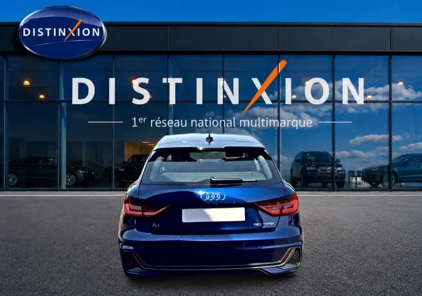 Vue arrière d'une Audi A1 Sportback 30 TFSI bleu foncé avec feux LED et becquet arrière, devant une vitrine Distinxion.